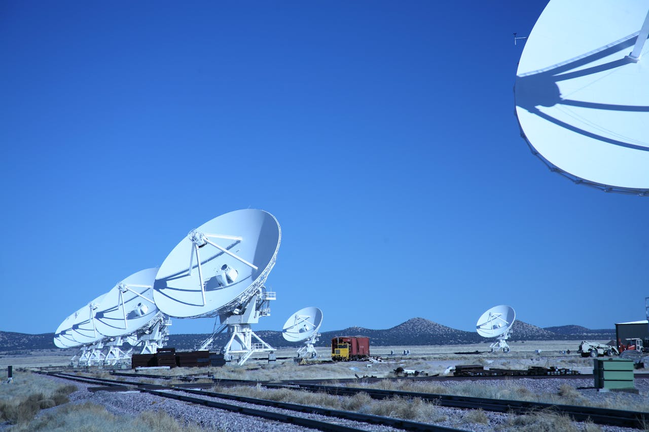 Multiple satellite dishes aligned in a field against a vibrant blue sky, showcasing modern communication technology.